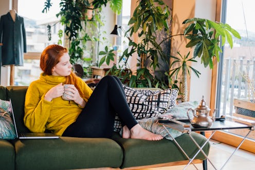 Young woman drinking tea on sofa as part of her seven day digital detox.