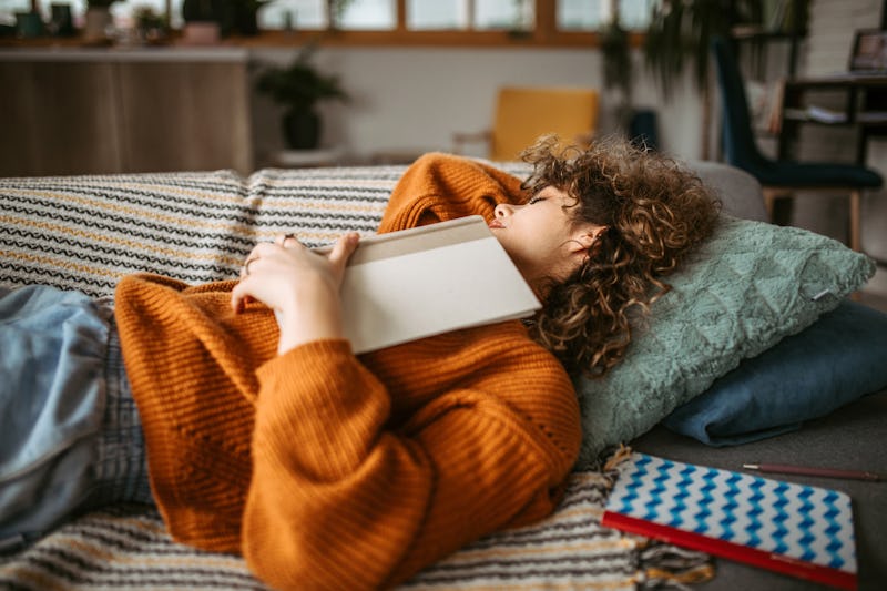 Young student woman taking a disco nap post-pandemic on the sofa in her living room after studying