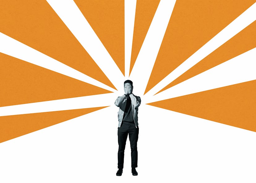 Depressed man covering face with hands while standing amidst orange rays against white background