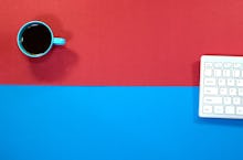 Office table with keyboard and Cup of Coffee on multicolored background.