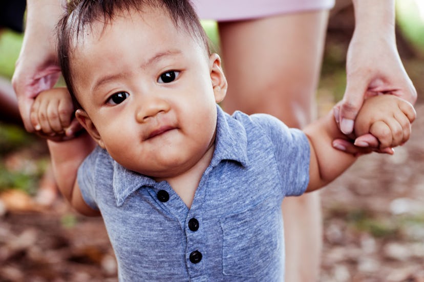 Front view of Southeast Asian baby boy learning to walk with his mother in a natural parkland