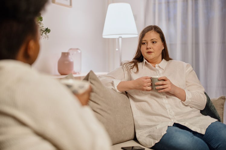 Two female friends talk about serious topics over a cup of tea at home. Roommates talking about ment...