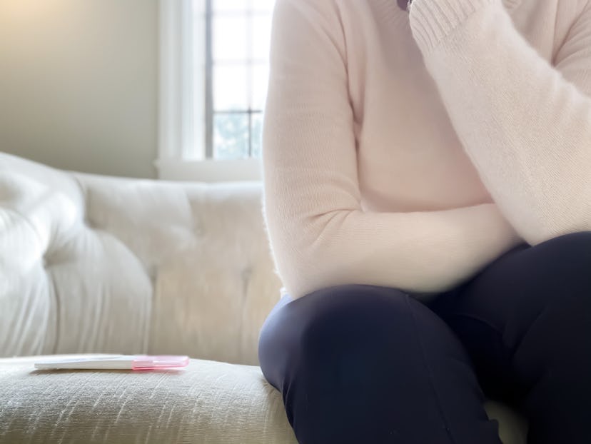 black woman waits with pregnancy test next to her on couch