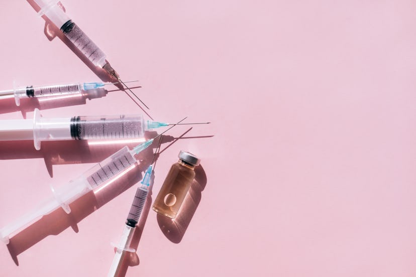 Top view of set of clean syringes placed near glass bottle of medicine with air bubble on pink backg...