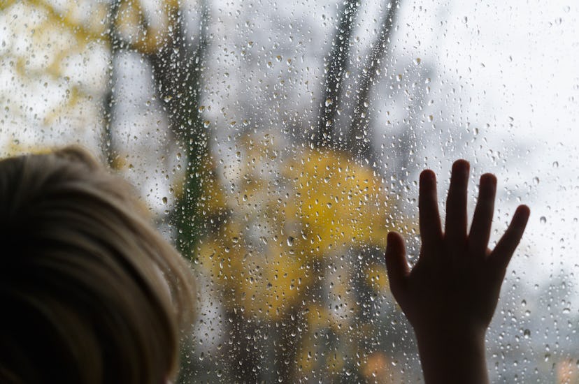 kid with hand pressed up to rainy window