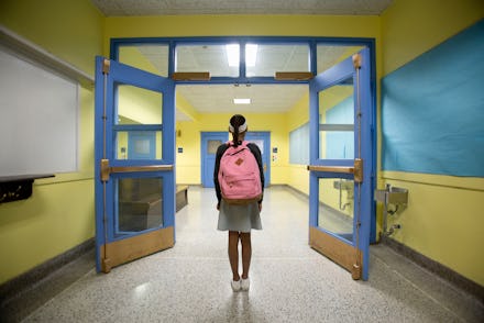 Rear view of eleven-year-old girl looking down school corridor.