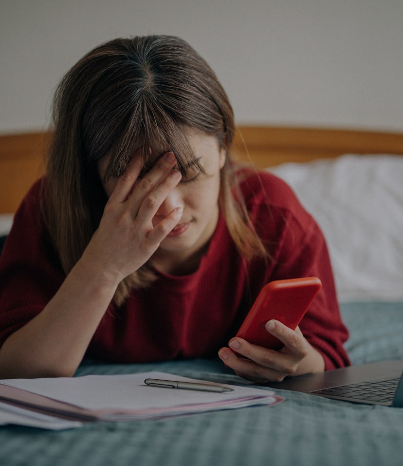 Tired overworked freelancer working with a smartphone and laptop in bed at bedroom.