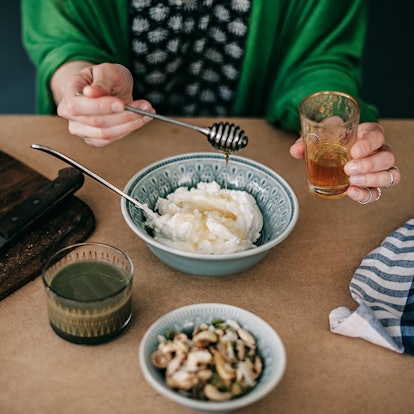 A woman spoons honey over yogurt, a food you can eat past its expiration date.