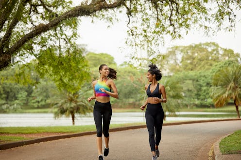 Smiling female looking at friend in park. Mid adult women are talking while jogging during summer. T...