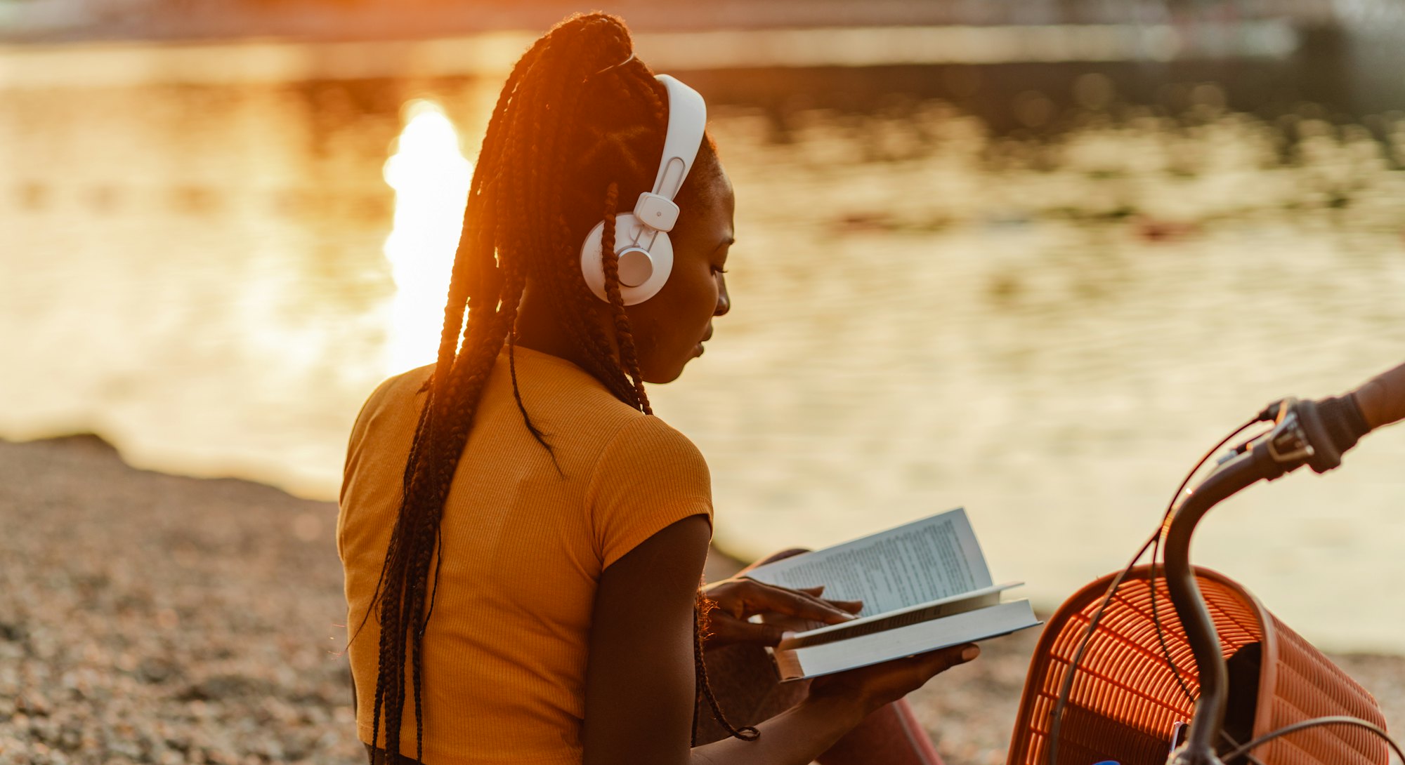 Photo of a young African American woman is using wireless headphones, she is sitting on the lakeshor...