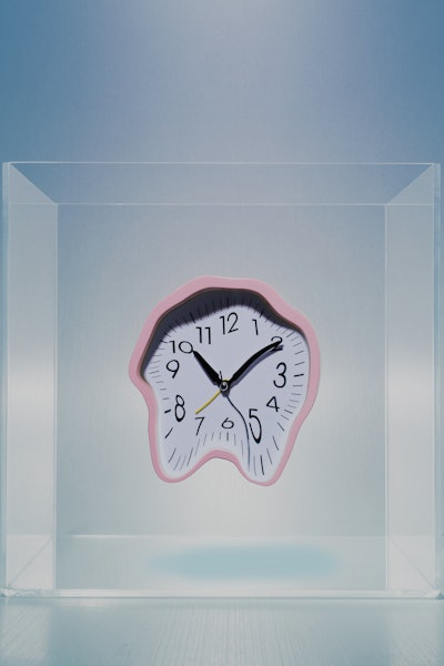 Melting pink analog clock in mid air inside of clear lucite cube