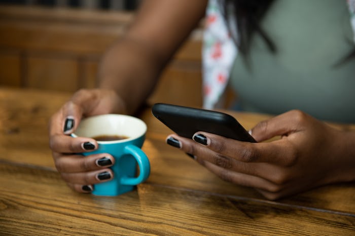Young woman sitting at a wooden kitchen table, looking at her smart phone