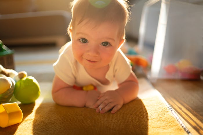 Portrait of a Caucasian baby boy with toys on the floor of his playroom looking at the camera.