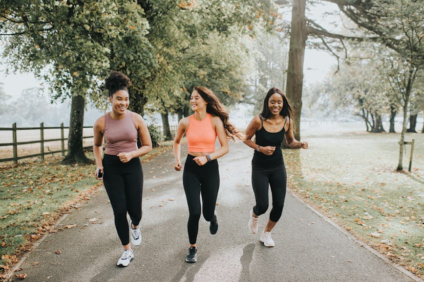 Strong, fit woman joggers, running through a sunny park. They chat and laugh as they exercise with e...