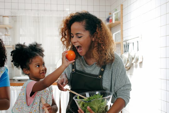 Daughter helping mom in the kitchen making a salad at home.