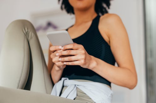 Unrecognizable young woman in leggings holding her phone and texting while waiting in the doctor's o...