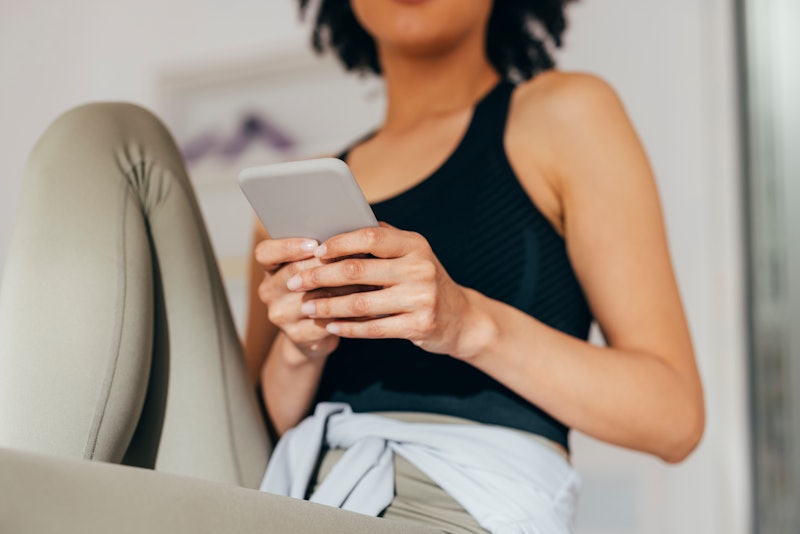 Unrecognizable young woman in leggings holding her phone and texting while waiting in the doctor's o...