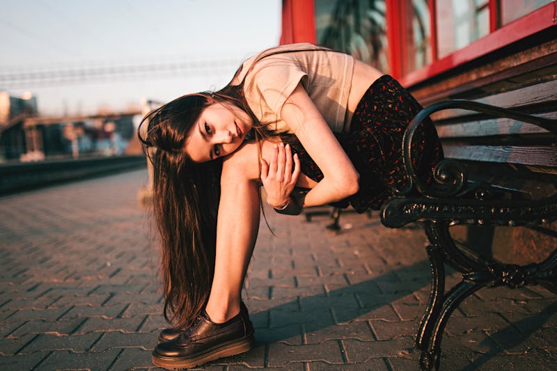 woman sitting in fetal position on a bench