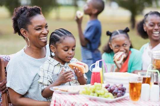 Two African-American adult sisters in their 30s with their three children at a backyard cookout. The...