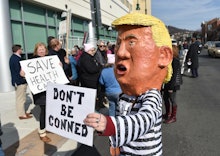 A protester in a Donald Trump costume holds a sign reading "Don't be conned". At the DoubleTree Hote...