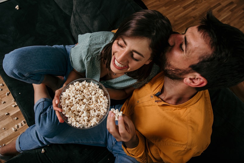 Upper view of a loving couple, enjoying evening time together by the TV, eating popcorn, and kissing...
