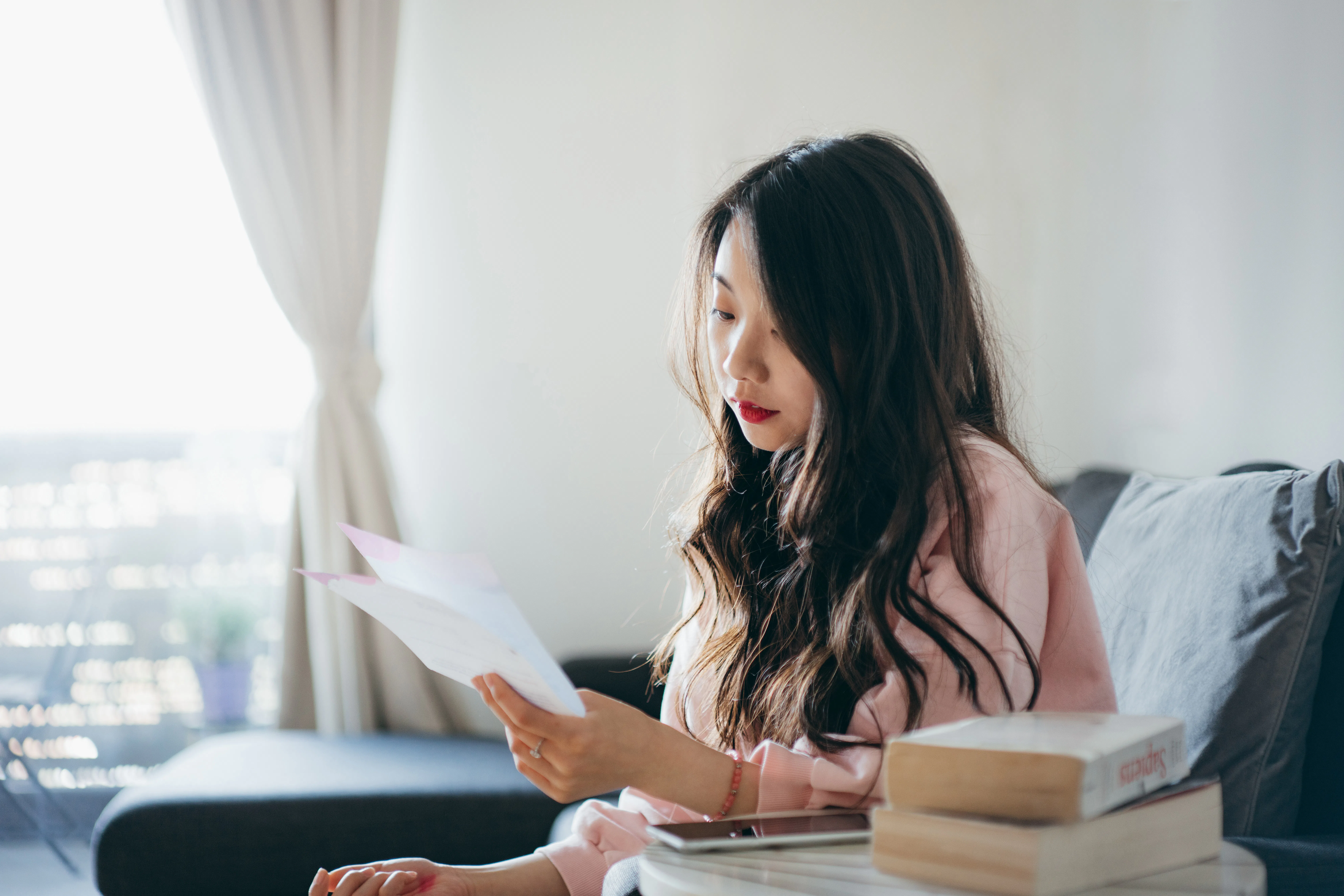 Young Asian woman sitting at home and thinking about how to take care of her bills with her smartpho...