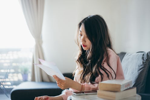 Young Asian woman sitting at home and thinking about how to take care of her bills with her smartpho...