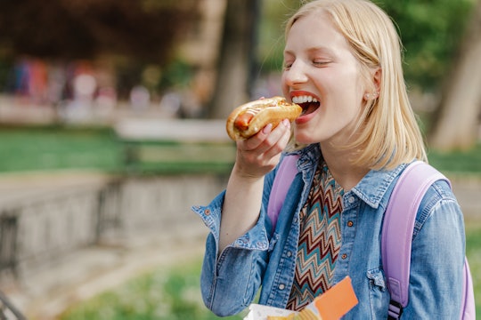 A young Caucasian woman is eating a hot dog and enjoying