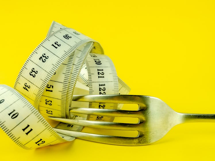 A fork with measuring tape wrapped around it in front of a yellow background