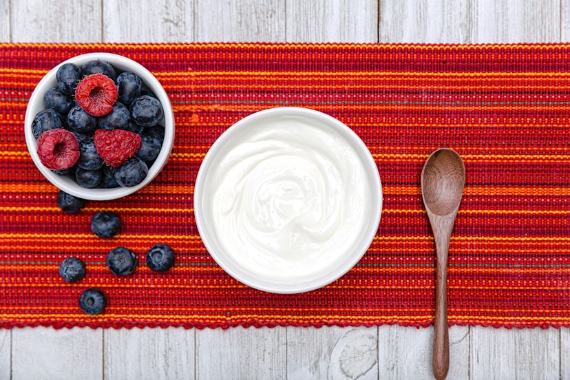 A bowl of plain Greek yogurt, and a bowl of fresh blueberries and raspberries on the table