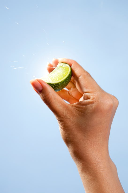 Asian woman squeezing a lime slice between her fingers with the blue sky and sunburst in the backgro...