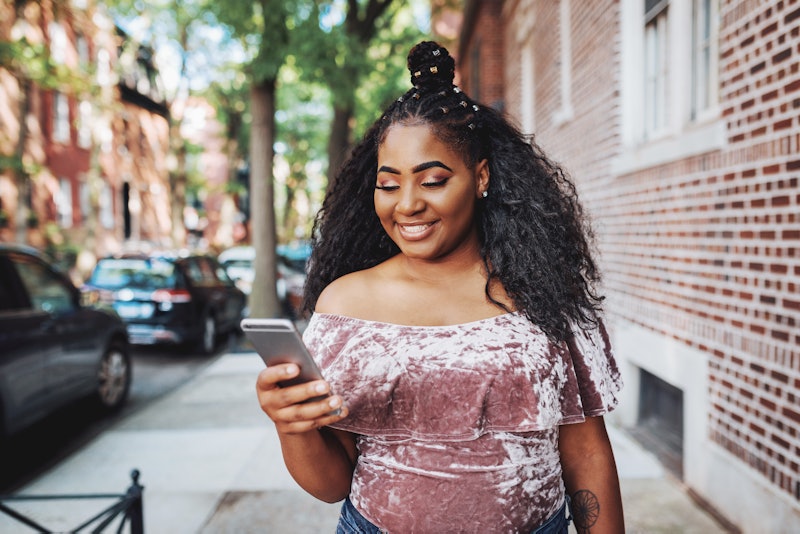 A woman in a crushed pink velvet top smiles at her phone. How to flirt via text, including all your ...