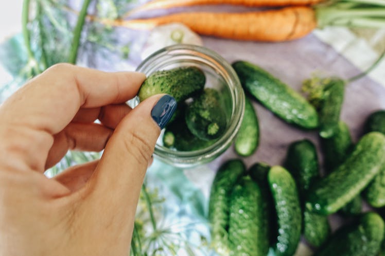 A young woman puts pickling cucumbers into a jar and follows a pickle recipe on TikTok.