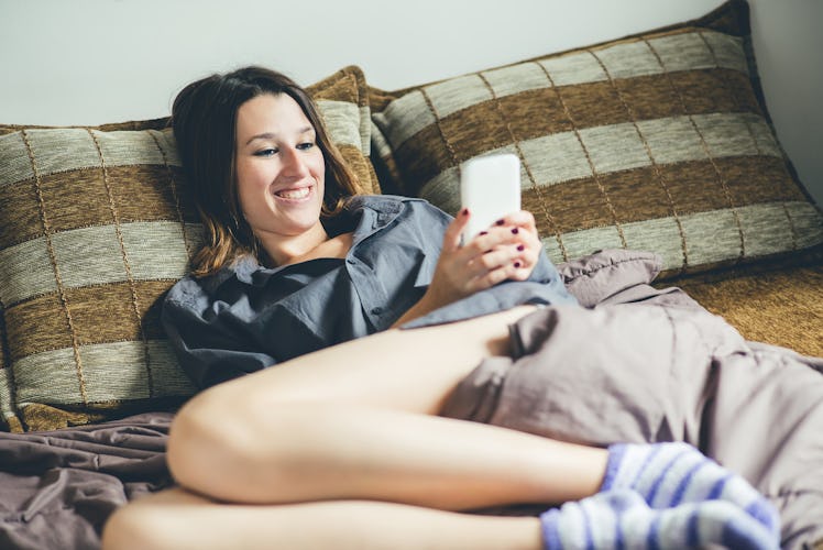 Woman resting in bed and using mobile phone.