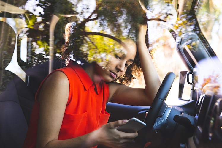 Woman with a orange colored dress pulled over the car and texting on mobile.
