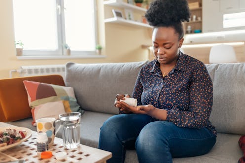 A woman sits on her couch measuring out supplements from a bottle. Experts explain the difference be...