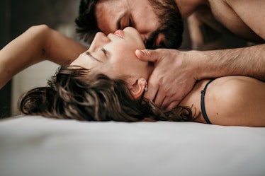 Side view photo of a beautiful couple in bed, being gentle and sensual. Handsome guy with a beard on...
