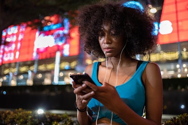 Teenage girl is listening music and typing message on smart phone in the city at night.