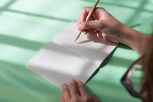 An over the shoulder view of young woman tracking her menstrual cycle on a note pad. Fertility aware...