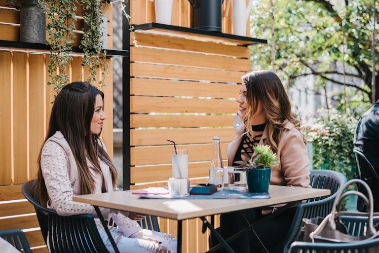 Two female friends having a conversation outside in a garden of a coffee shop