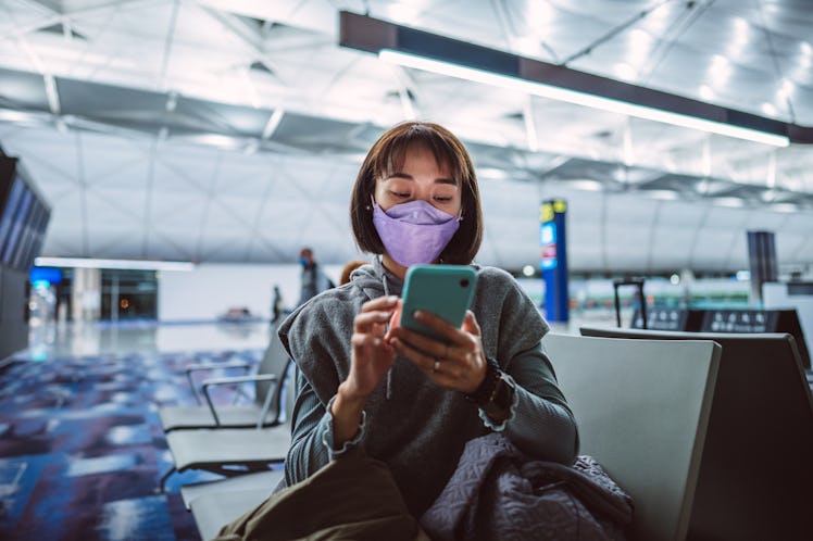 A young woman preps a vaxication selfie post on her phone while sitting in the airport.