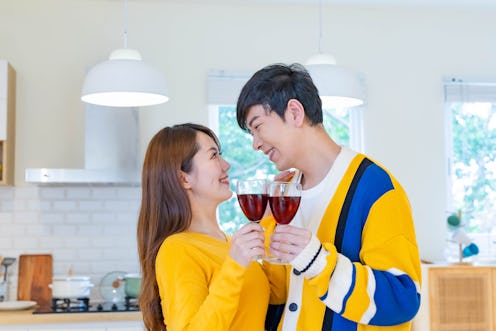 asian couple are looking at each other and smiling with red wine while celebrating anniversary in th...