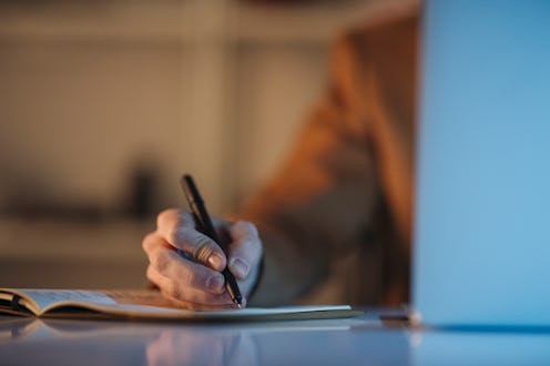 Man is sitting using his laptop and writing notes in his notebook