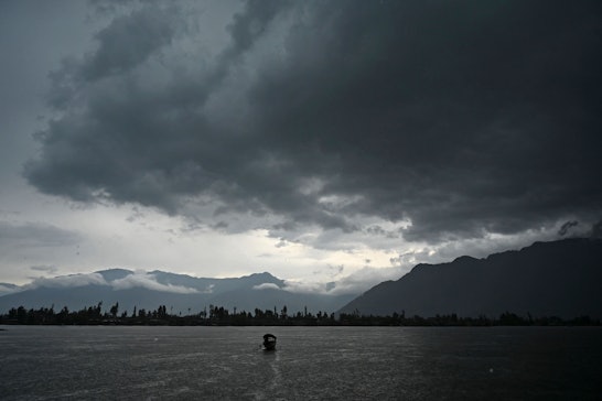 A man steers a boat as dark clouds loom over Dal Lake during a rainfall in Srinagar on June 1, 2021....