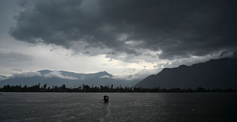 A man steers a boat as dark clouds loom over Dal Lake during a rainfall in Srinagar on June 1, 2021....