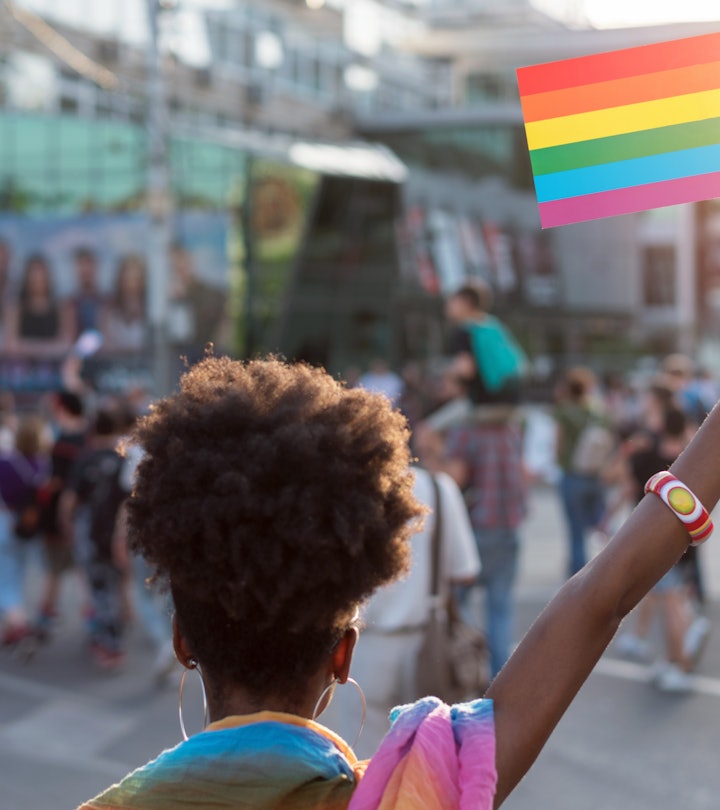 Rear view image of young African ethnicity woman walking at the LGBTQI pride event and waving rainbo...