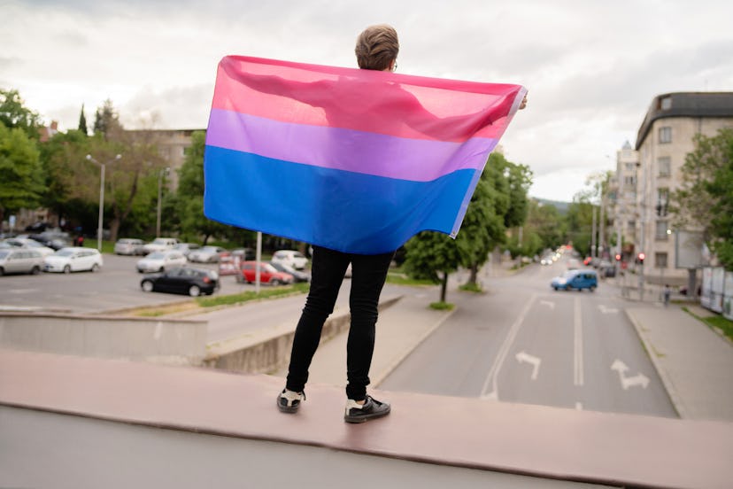 A bi woman holds up the bisexual pride flag: pink, purple, and blue.
