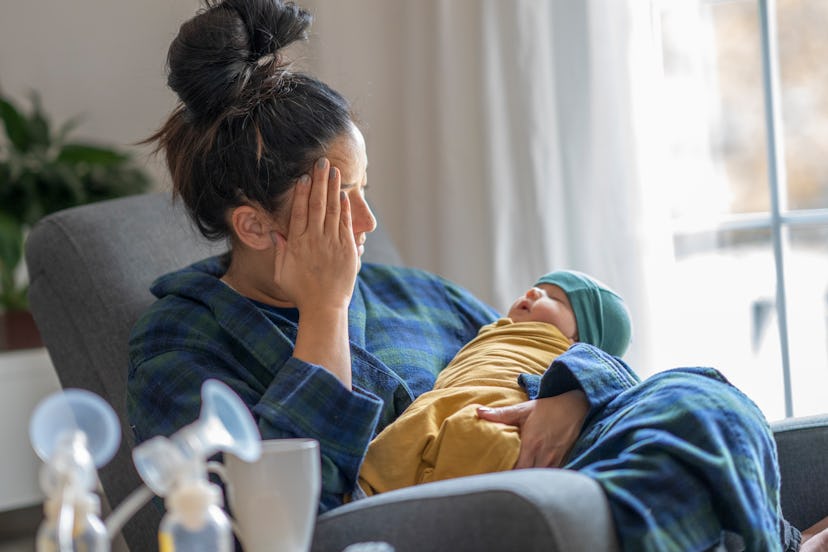 Tired mother with postpartum depression holding her newborn child at home after tying to pump.