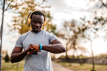 Athlete check fitness tracker on smartwatch or playing his music playlist after training in nature.