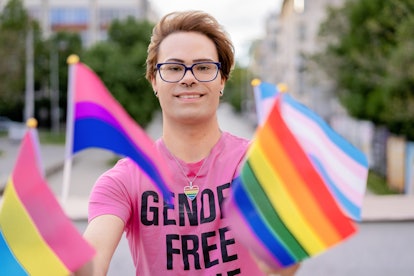 LGBTQ+ activist holding different flags of LGBTQI community defending the human rights, looking at c...